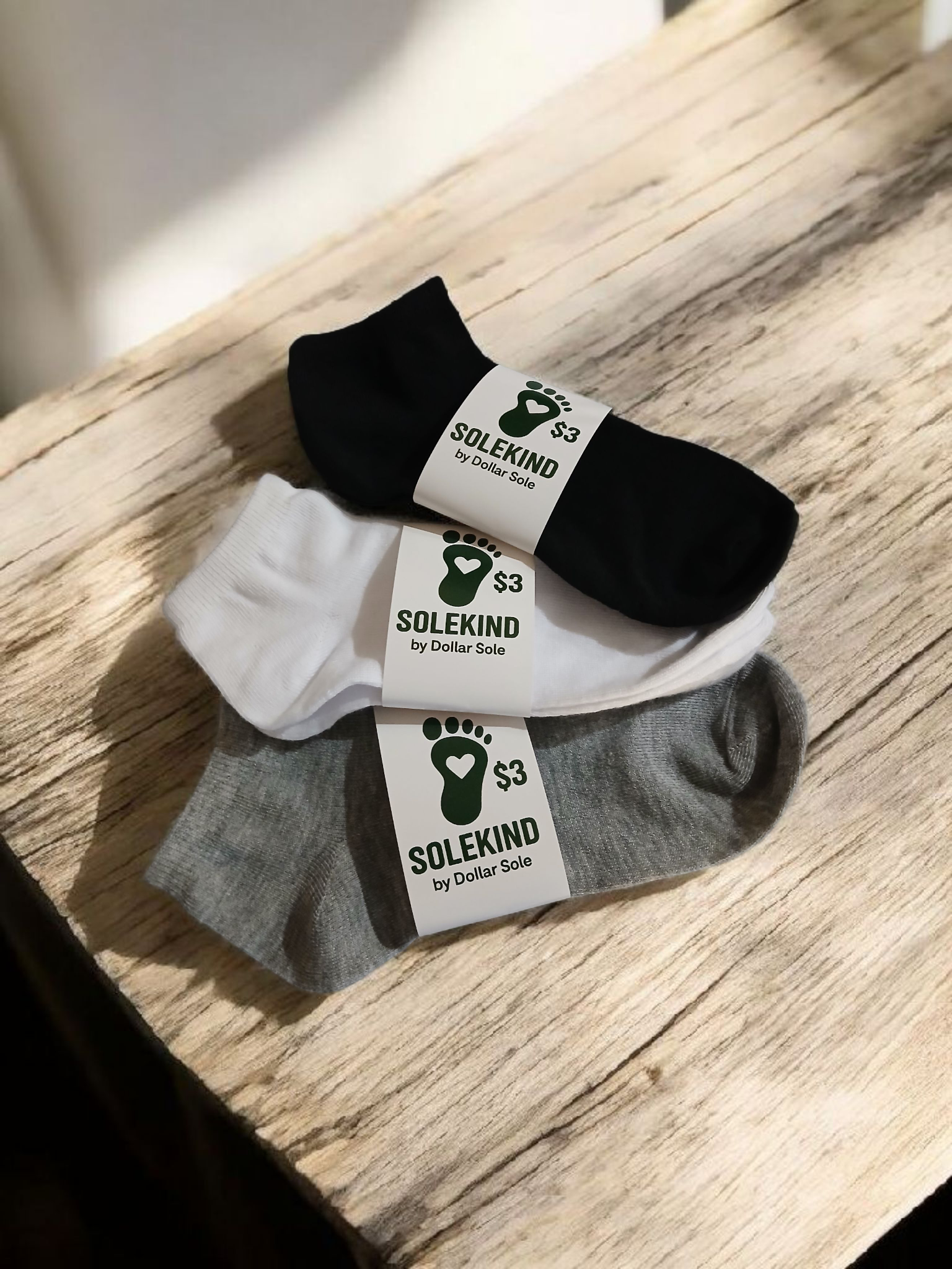 Three pairs of white, black and gray polyester SoleKind ankle socks for men, shown folded or laid flat.